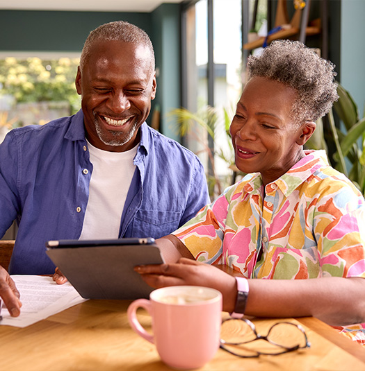 smiling senior couple on their ipad at the kitchen table researching annuity for retirement